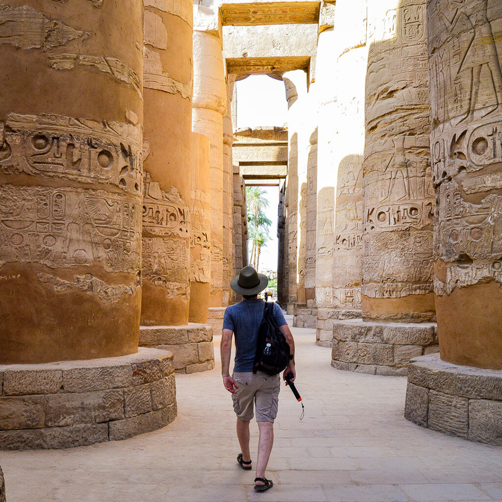 A low angle shot of a male walking between columns in Karnak Temple in Egypt
